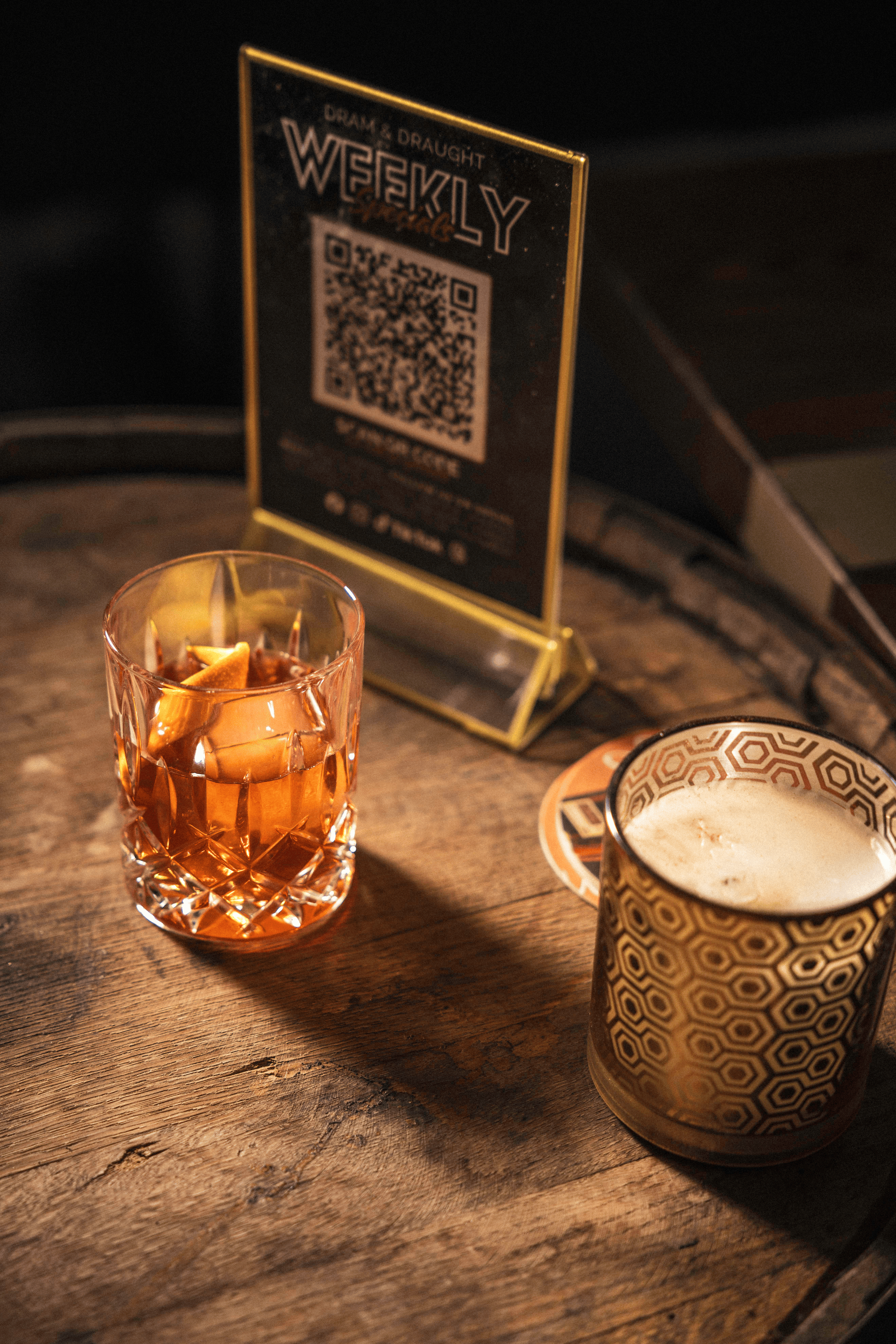 Craft cocktails on a rustic wooden table, featuring a crystal glass filled with vibrant orange drink and a patterned mug.